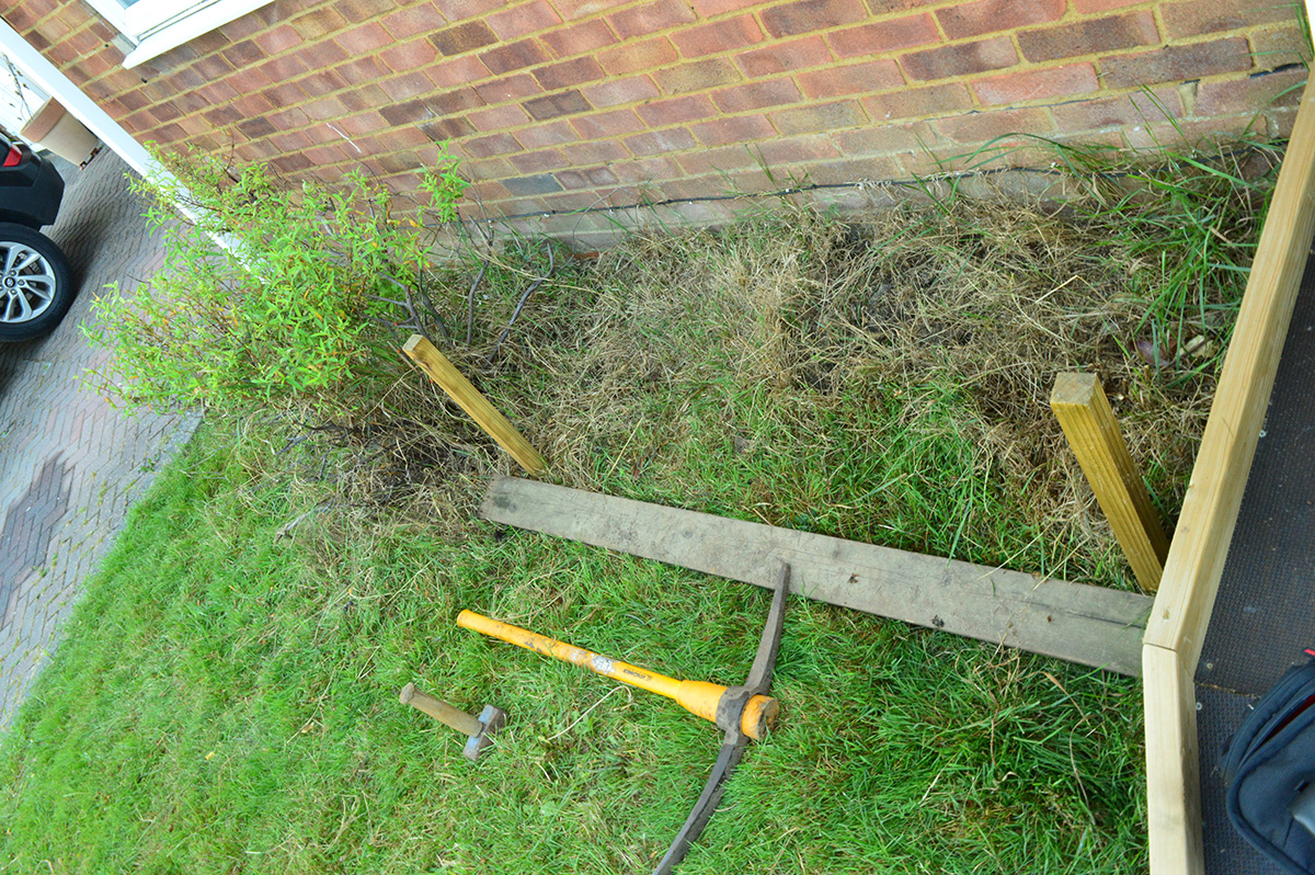 a flowerbed overgrown with grass and weeds. hammer, pickaxe, wooden stakes